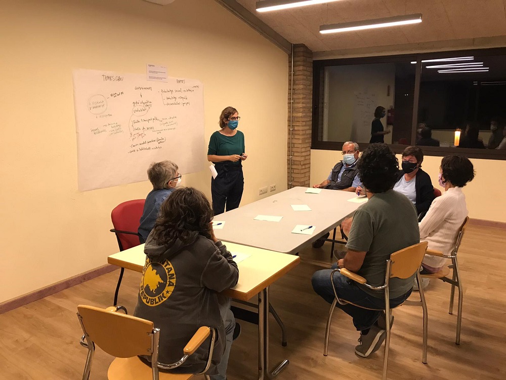 Aula formativa amb persones assegudes en cercle i la formadora de peu davant la pissarra