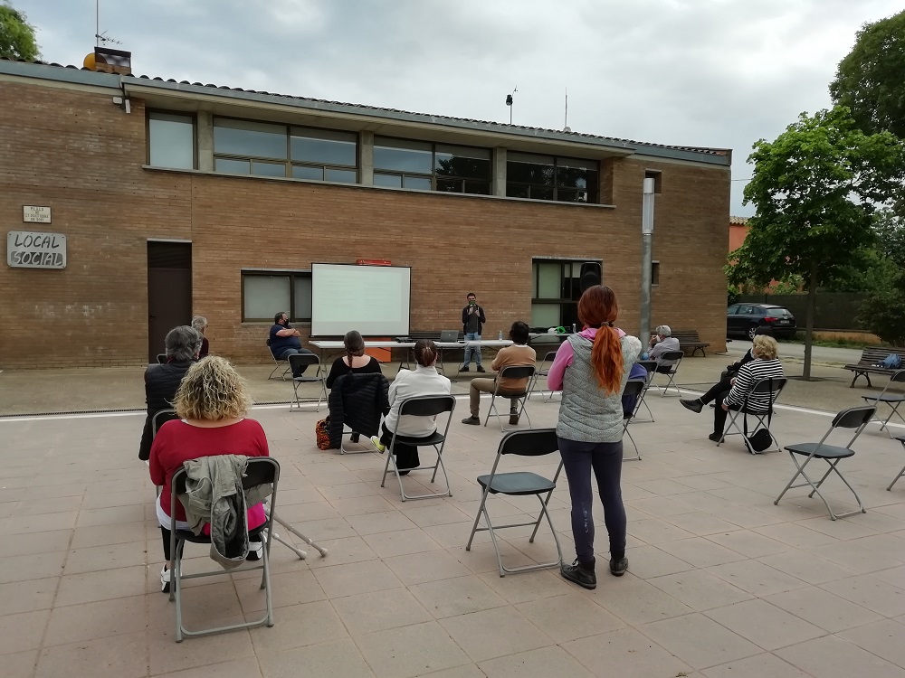 Conferència a l'exterior d'un edifici amb l'audiència d'esquenes i la imatge projectada al davant