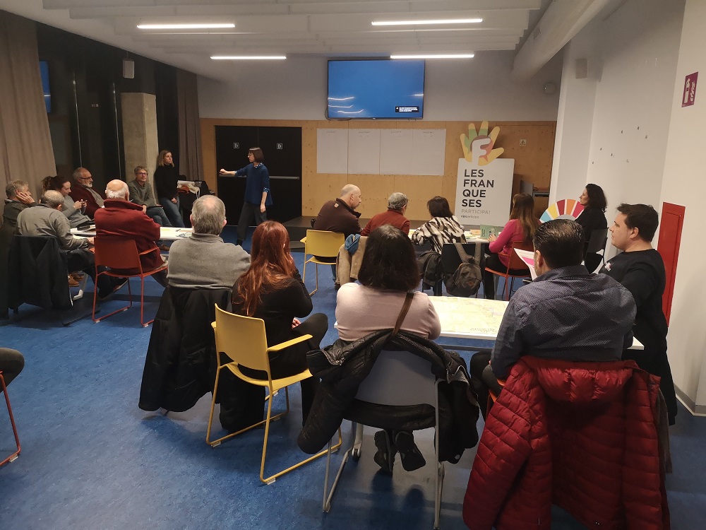 Aula formativa amb persones assegudes i la formadora de peu davant la pissarra