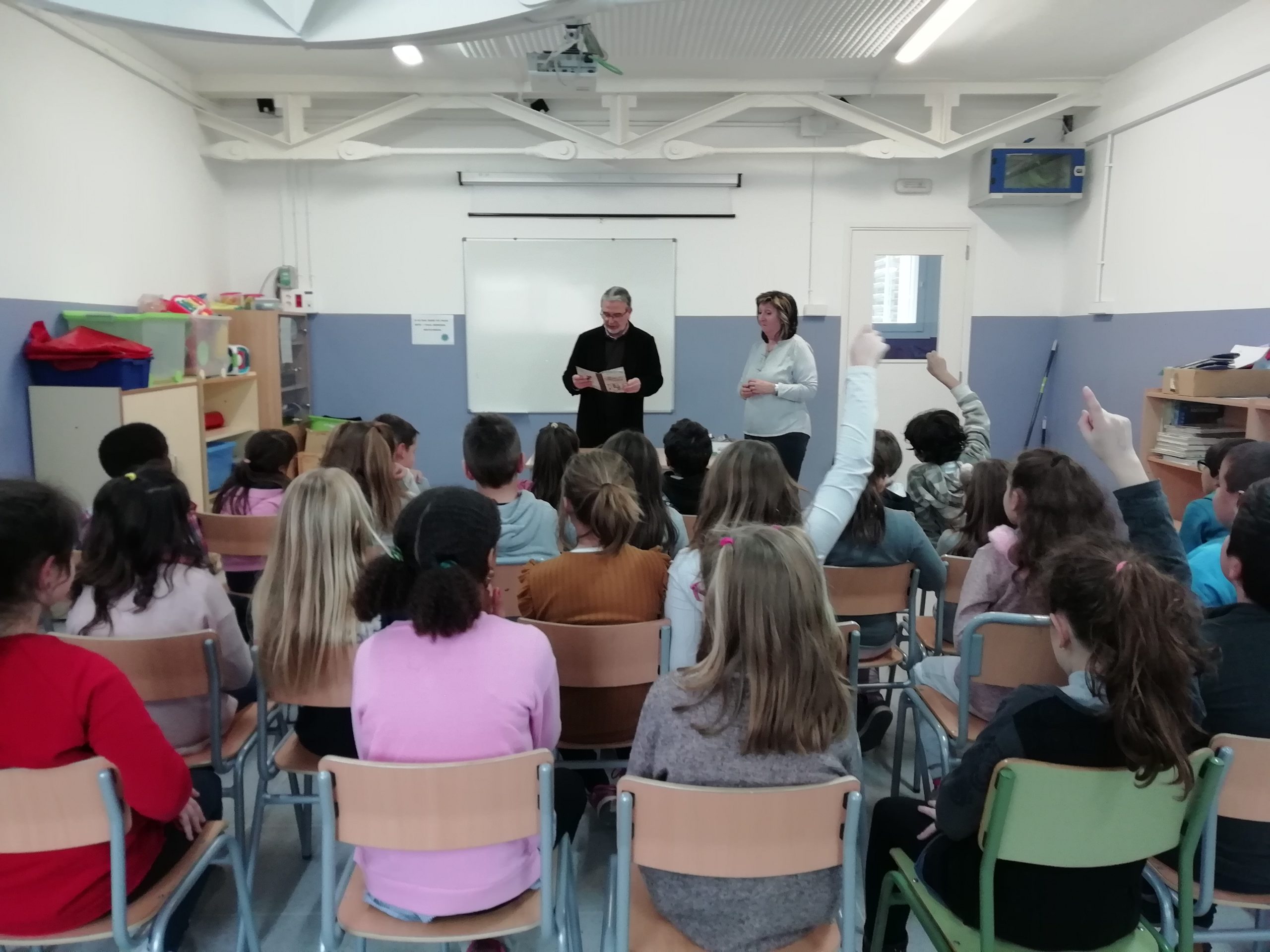 Aula formativa amb infants asseguts d'esquenes mirant a dos formadors