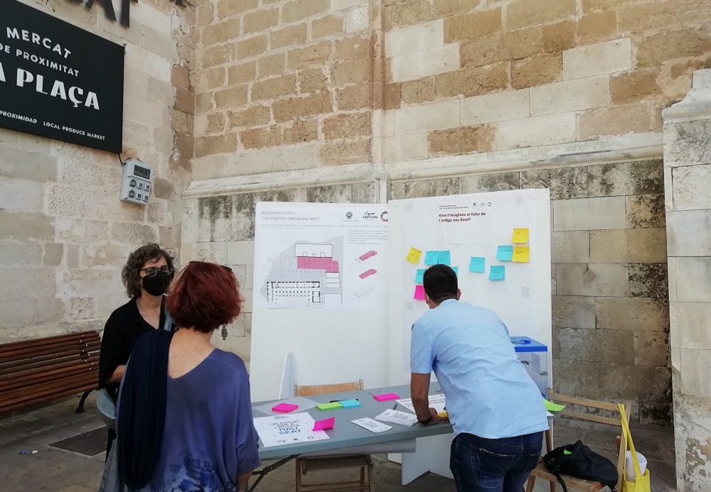 Persones a la taula d'una fira amb notes de postit en un mural