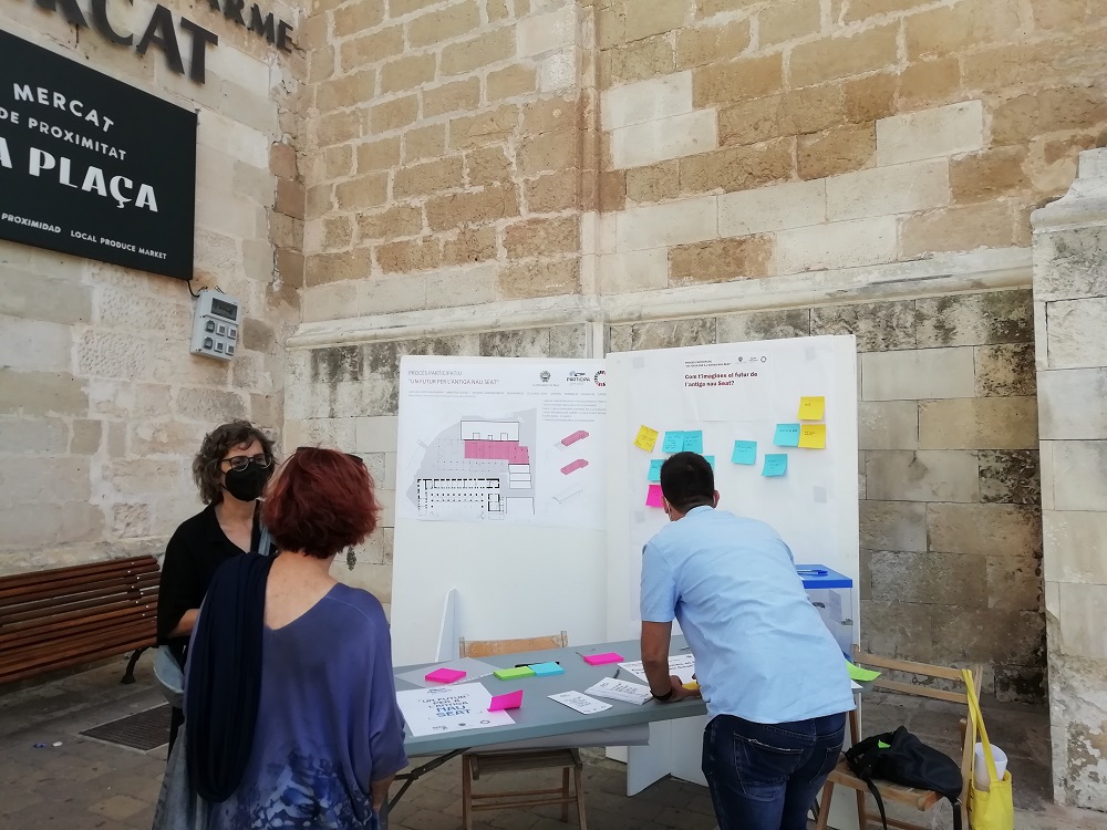 Persones a la taula d'una fira amb notes de postit en un mural