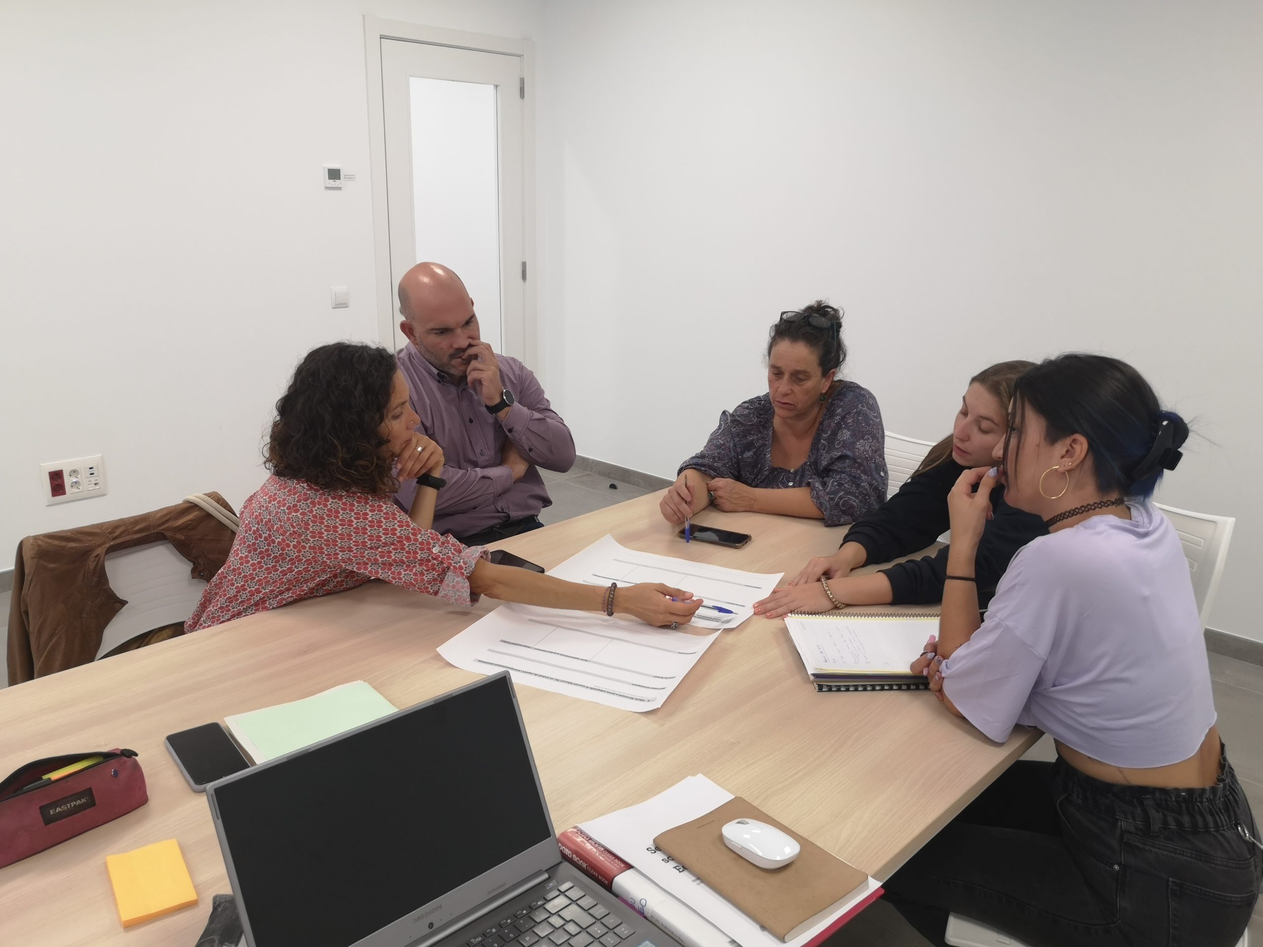 5 persones en cercle compartint un paper amb un esquema